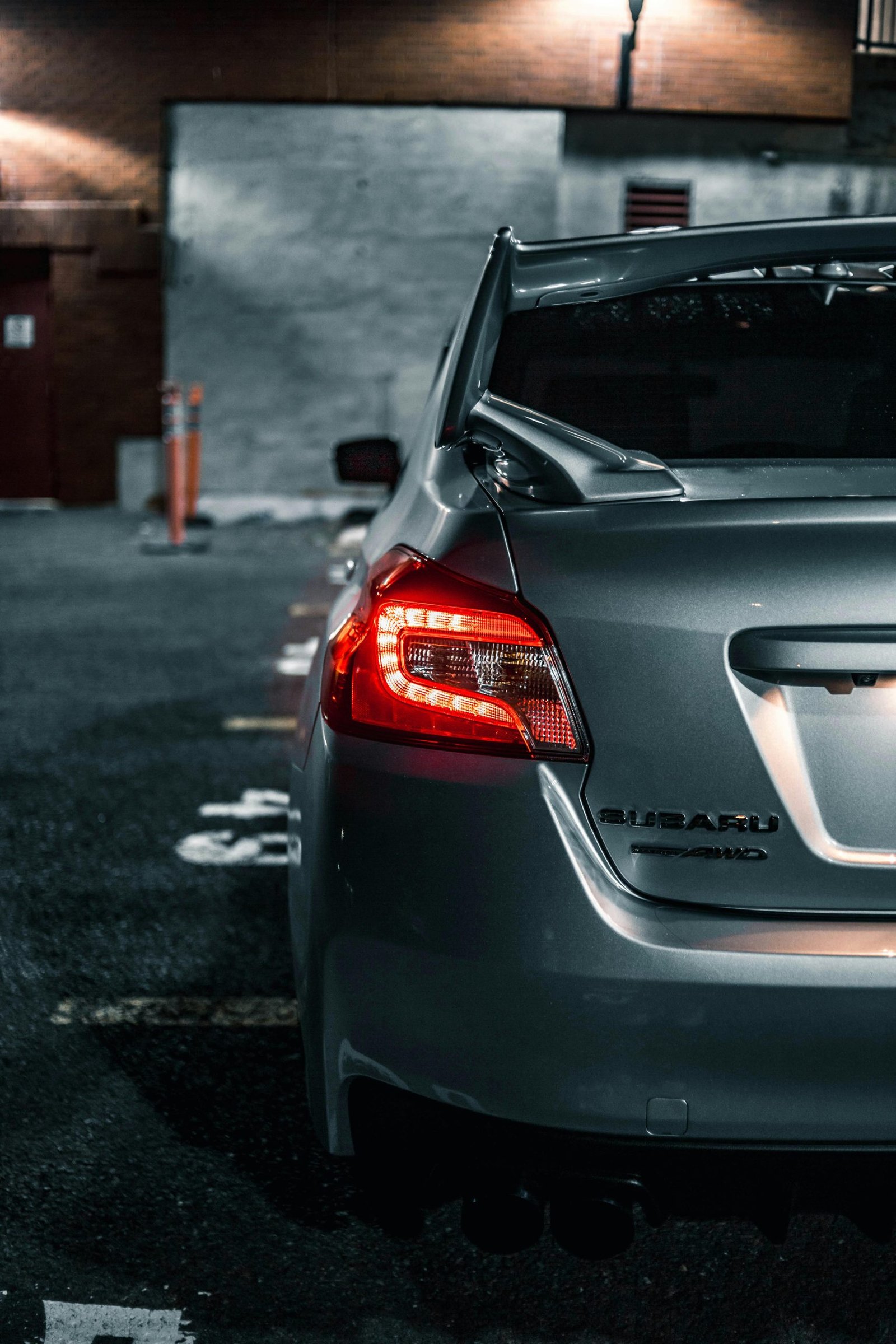 Close-up of a Subaru car's illuminated taillight in a dimly lit urban parking area.